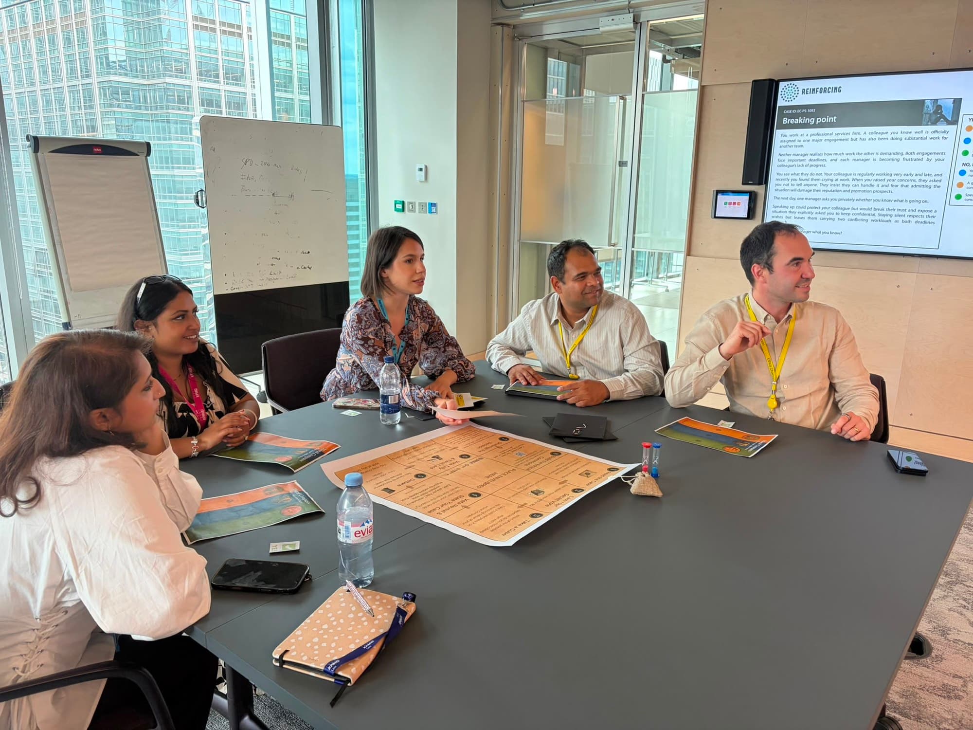 Five people around a boardroom table at KPMG, the ethixCube board and case cards spread between them, a case brief on the screen behind